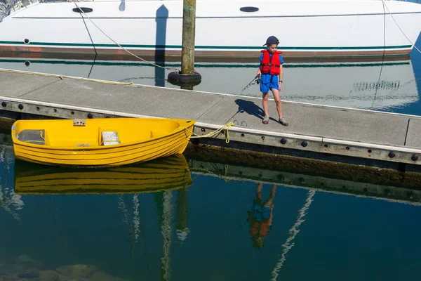 码头小男孩钓鱼黄色小艇反映在水中 — 图库照片