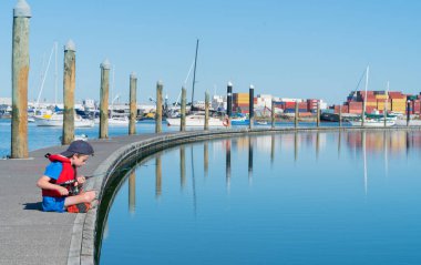 Uzun kıvrımlı pier rıhtım balıkçılık Tauranga Harbour Yeni Zelanda üzerinde oturan kırmızı can yeleği küçük çocukla mavi sakin su çevrili.