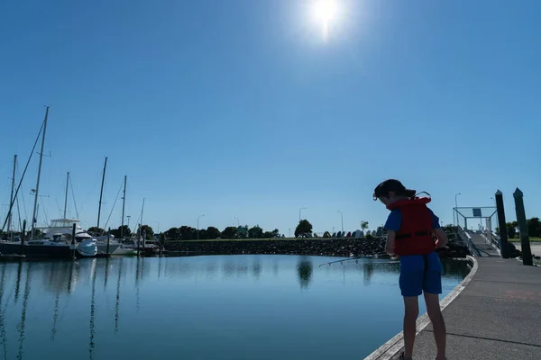 小男孩在阳光明媚的早晨阳光下 穿着红色救生衣从码头钓鱼 — 图库照片