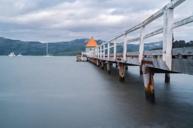 Daly's Wharf veya Akaroa döken ve turuncu ile Akaroa Limanı İskele yuvarlak sonunda uzun pozlama ve yavaşça su sallanan dan mesafe bulanık teknelerle konik çatı.