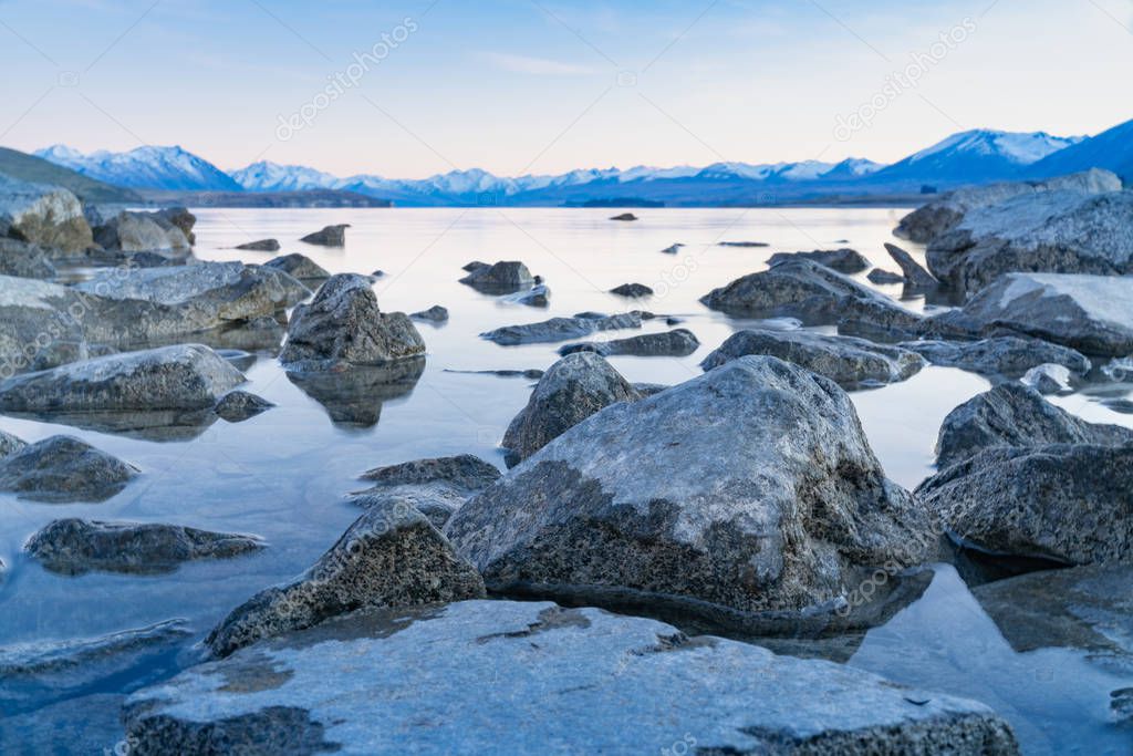 Lake Tekapo sunsise over rocky foreshore and low water level of calm peaceful lake