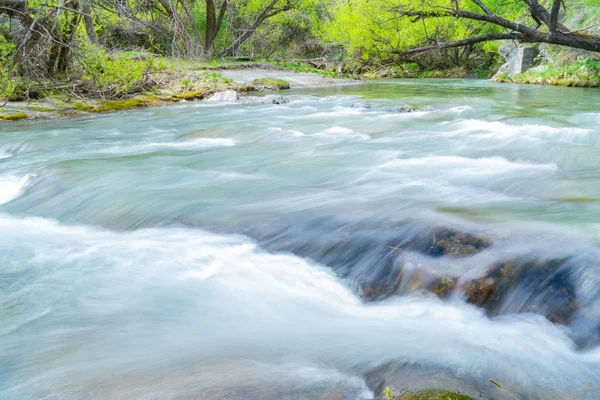 Long exposure Arrow River flowing fast through gorge lined with lush green deciduous trees