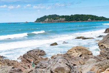 Mount Maunganui Yeni Zelanda - 8 Şubat 2019: Kayalar ve haddeleme sörf dalgalar arasında günlükken insanlarla daha düşük Mount Maunganui Rocky kenarına içinde ötesinde.
