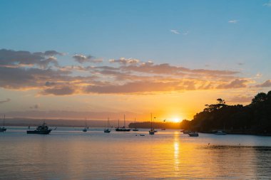 Tauranga Harbour körfezde Pilot üzerinde güneş kümeleriyle tekneleri ve Mount Maunganui siluet olarak doğal uzak manzara