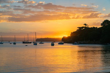 Tauranga Harbour körfezde Pilot üzerinde güneş kümeleriyle tekneleri ve Mount Maunganui siluet olarak doğal uzak manzara