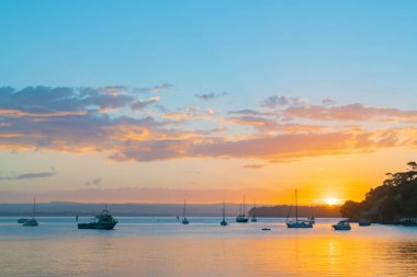 Tauranga Harbour körfezde Pilot üzerinde güneş kümeleriyle tekneleri ve Mount Maunganui siluet olarak doğal uzak manzara
