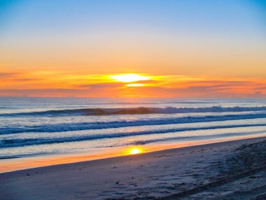 Geniş plaj görüntüsü olarak güneş bulutların üzerinde ufuk üzerinde yükselir.