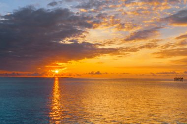 Sunrise glow across ocean framed by dark clouds clipart