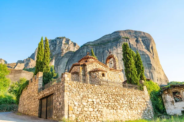 De grands rochers imposants s'élèvent derrière l'église grecque pittoresque en pierre — Photo