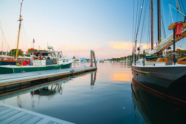 Розовый и диапазон свечения заката цвета отражается на спокойной воде в гавани с классическими линиями кетча, ведущих от пирса в залив
.