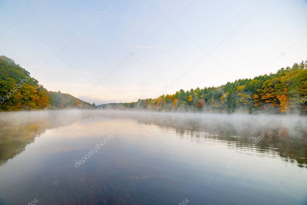 Scenic early morning fog just above the water level of Connecticut River with colorful fall foliage along both sides converging into distance.