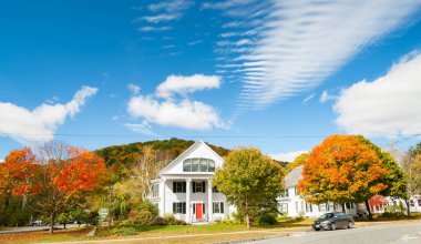 Geleneksel Amerikan beyaz ahşap esnek mimarisi ile sokak sahnesi parlak renkli sonbahar yapraklarıyla çevrili ve mavi gökyüzü altında. Newfane, Vermont, ABD.