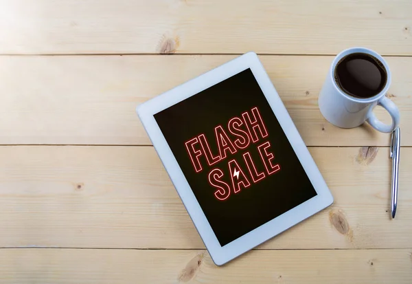 Flash sale text in neon style on tablet with coffee mug on wooden table