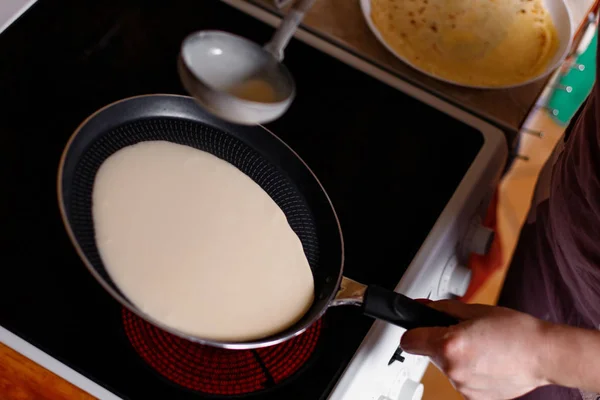 Grandmother is cooking pancakes in a frying pan. The cooking process in the kitchen.