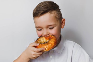 Tatlı bir çocuk haşhaş tohumu ile lezzetli, taze pişmiş ekmek yiyor. Çocuk beyaz bir arka plan üzerinde hamur işleri var.