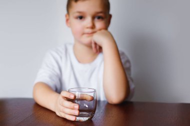 Mutfakta masada boş bir bardak ile üzgün küçük bir çocuk oturur. Adam üzgün görünüyor.