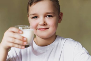 Oğlu sabah mutfakta süt içiyor. Genç bir çocuk bir sınıf, lezzetli, ev yapımı süt gösterir. Sağlıklı kahvaltı.