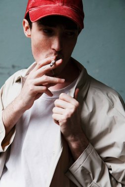 Sigara kırmızı beysbol şapkası ve yağmurluk genç bir adam portresi. Moda portre modeli. Beyaz gömlekli bir adam.