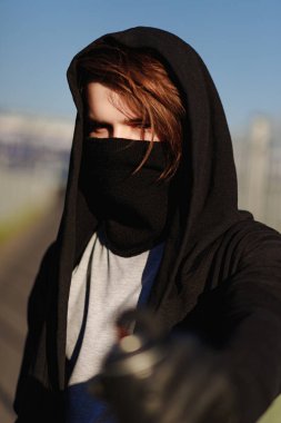 Şehir arka plan üzerinde bir maskeli genç bir adam portresi. Kukuletalı Vandalist ve sprey boya ile el olabilir