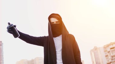Kukuletalı adam maskesi çizim grafiti tarafından sprey boya ile olabilir. Grafiti sanatçısı çiziyor. Aerosol vandalizm portre. Kentsel kavramı. Günbatımı