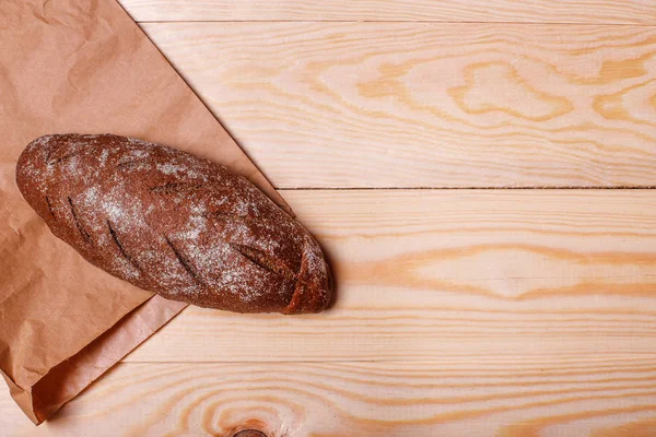 Rye loaf bread on paper bag and wood background. Top view. Text space