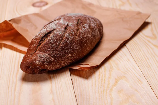 Homemade bread on paper bag. Baked product on wooden table. Close view