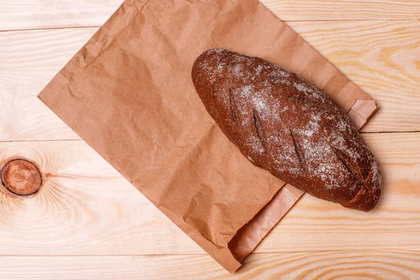 Tasty black bread and paper bag on wooden background. View from above. Space for text