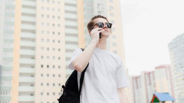 Telefonuyla konuşan öğrenci. Beyaz gömlek, güneş gözlüğü kentsel tarzı