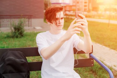 Güzel çocuk oturur ve yeşil park telefonuna fotoğraf çekmek. Açık