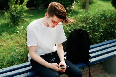 Kırmızı gözlük yakışıklı öğrenci parkta oturur ve telefonunu kullanın