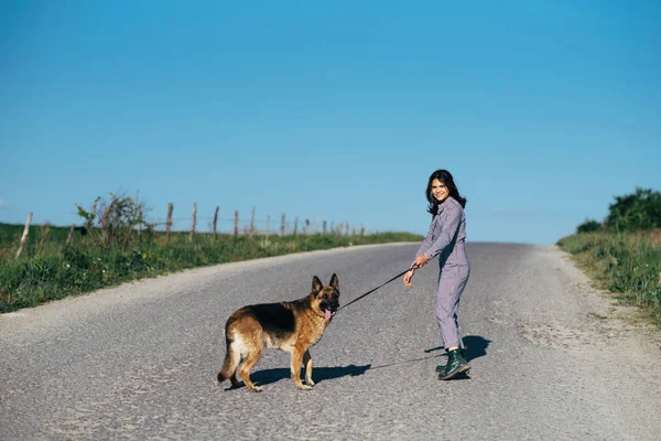一个漂亮的女孩在路上领着一条狗在她身旁 — 图库照片