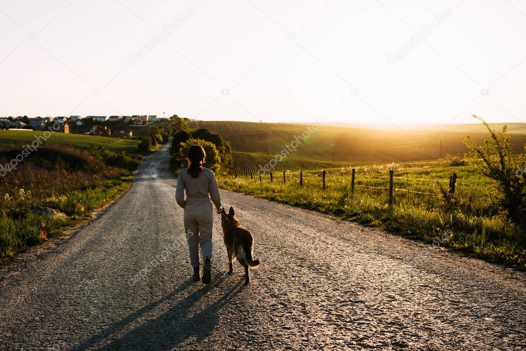A pretty girl leads a dog next to her on the road.