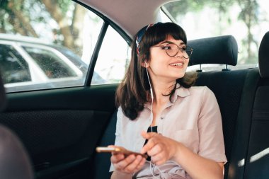 Güzel genç güzel kız bir akıllı telefon kullanarak ve arabanın arka koltukta otururken gülümseyen.