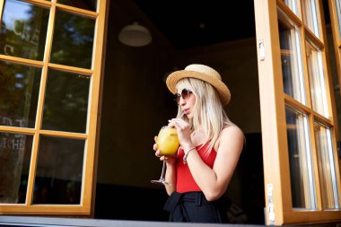 Bir genç, sempatik sarışın açık bir pencere yakınında bir kafede anlamına gelir ve bir kadeh kokteyl tutar