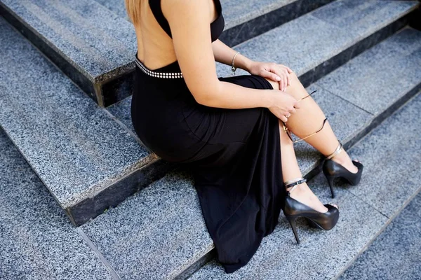 Hermosas chicas piernas en un vestido negro, sentado en las escaleras —  Fotos de Stock