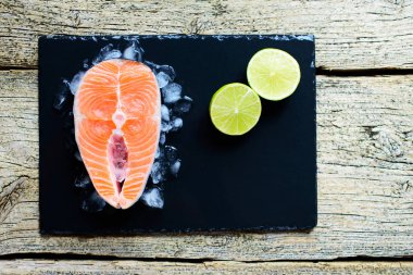 Somon biftek buz üzerinde siyah ahşap masa üstü kireç ile görüntüleyin. Balık gıda kavramı. Kopya alanı.