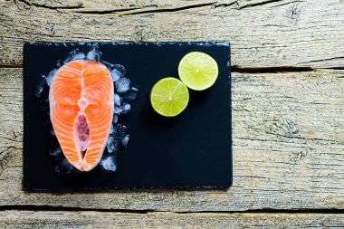 Somon biftek buz üzerinde siyah ahşap masa üstü kireç ile görüntüleyin. Balık gıda kavramı. Kopya alanı.