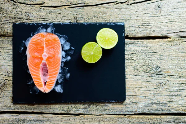Somon biftek buz üzerinde siyah ahşap masa üstü kireç ile görüntüleyin. Balık gıda kavramı. Kopya alanı.