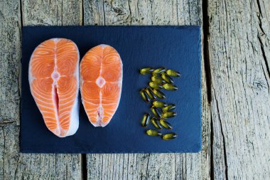 İki somon biftek yalan bir kara tahta üzerinde ve orada yanında vitamin vardır. Üstten görünüm. Vitamin almak için seçim.