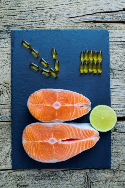 İki somon biftek yalan kireç ve orada yanında bir parça ile kara bir tahta üzerine vitamin vardır. Üstten görünüm. Vitamin almak için seçim.