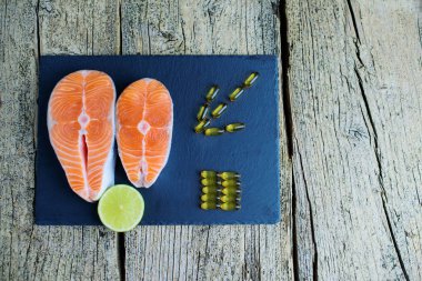 İki somon biftek yalan kireç ve orada yanında bir parça ile kara bir tahta üzerine vitamin vardır. Üstten görünüm. Vitamin almak için seçim.