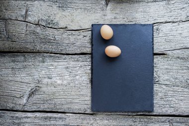 Ahşap arka plan üzerinde siyah bir gemide iki çiğ tavuk yumurtası yalan.