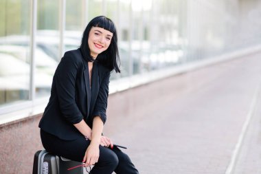 Genç güzel bir takım elbise ve gözlük ile telefonda konuşurken bir bavul giymiş ve fotoğraflandı kız.