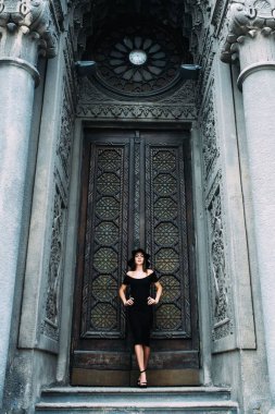 Sevimli Genç kız büyük güzel kapı siyah elbise ve şapka zemin karşı poz görünüm modelleme.