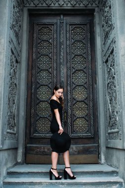 Sevimli Genç kız büyük güzel kapı siyah elbise ve şapka zemin karşı poz görünüm modelleme.