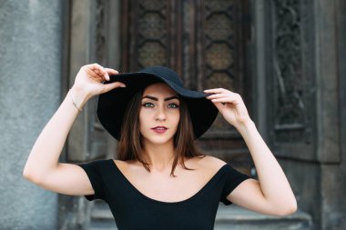 Sevimli Genç kız büyük güzel kapı siyah elbise ve şapka zemin karşı poz görünüm modelleme.
