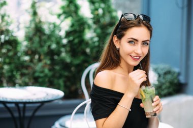 Genç güzel kız sokakta bir kafede oturan ve içme içki soğutmalı.