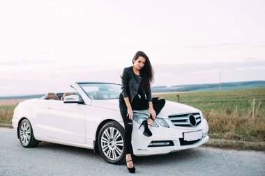 Pantolon ve beyaz cabriolet araba için bekleyen bir deri ceket giymiş kadın çok güzel.