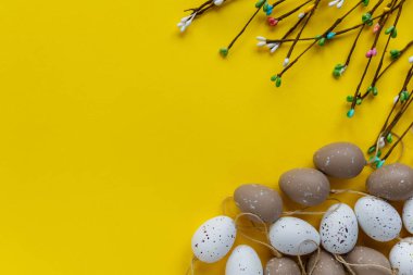Easter decor. The branches of willow and decorative eggs are laid out on an yellow background clipart
