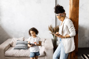Oturma odasında ayakta iken sevimli bir anne ve kızı konuşma ve tablet bakmak